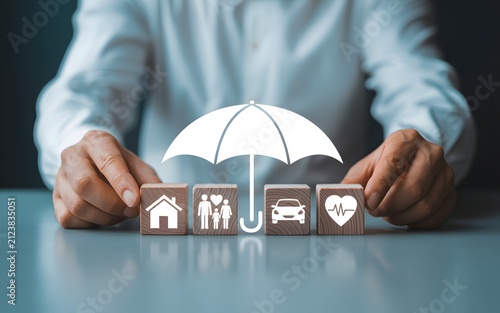 Insurance coverage concept with protective umbrella icon over wooden blocks featuring family home car and heart.