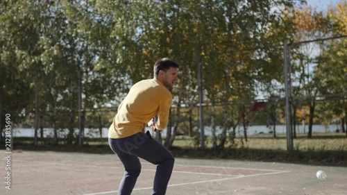Dynamic shot of man playing pickleball outdoor. Slim guy actively and quickly hitting perforated ball on court in park on sunny day, handheld shot. Energetic gameplay, speed, control, precision.