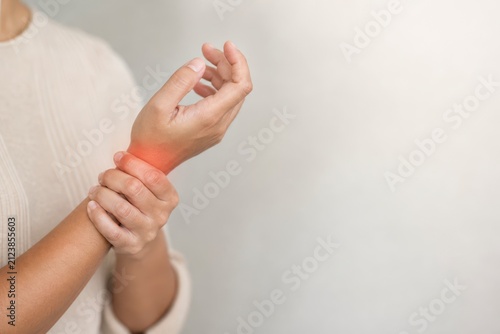 Woman Experiencing Wrist Pain Grasping Her Hand in a Light-Filled Space with a Neutral Background