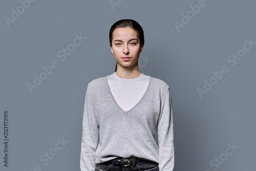 Portrait of a serious 18-year-old young woman on grey studio background