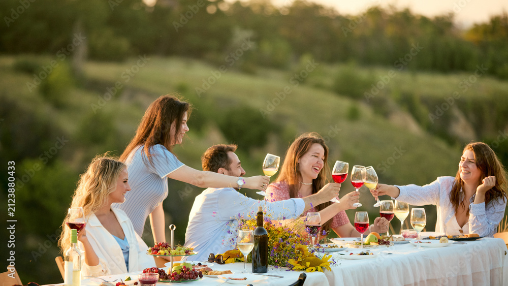 Obraz premium Women reaching across outdoor table to clink wine glasses in celebration. Concept of female community, friendship campaign, celebratory beverage marketing.