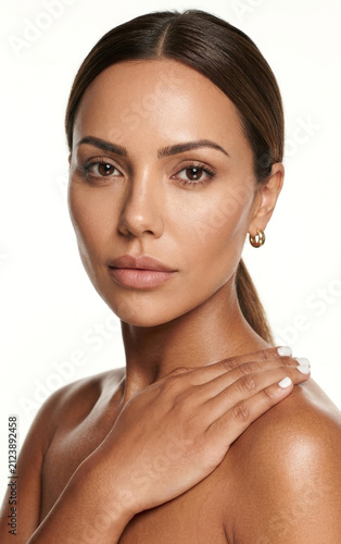 Radiant beauty portrait of a woman with a sun-kissed, glowing complexion and sleek dark hair pulled back into a neat ponytail