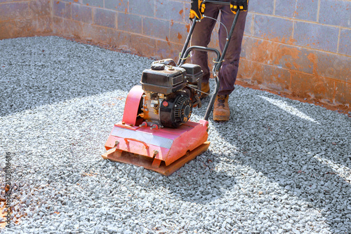 Fotografie Worker operates vibration plate compactor to flatten gravel at construction site