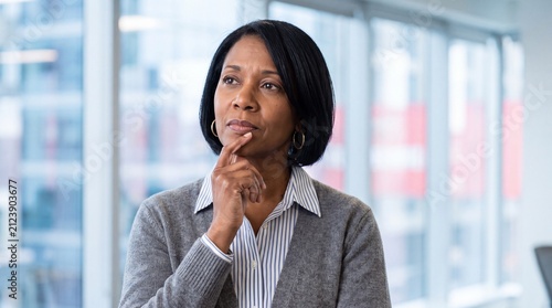 Thoughtful mature businesswoman with hand on chin looking away in a modern office