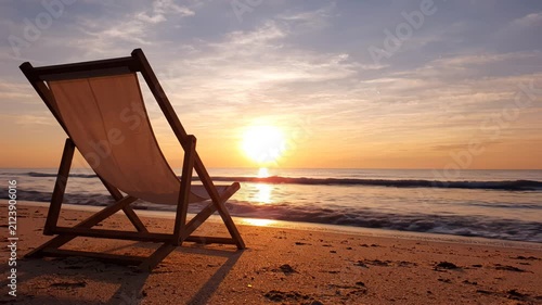 Empty beach chair facing sunset over ocean waves at golden hour, tranquil seaside relaxation scene