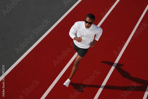 Athletic man sprinting on red track with white lines, dynamic running pose, intense focus, athletic performance, vibrant sportswear, outdoor stadium lighting