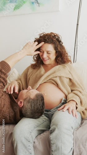 Affectionate Latin couple resting on couch during pregnancy