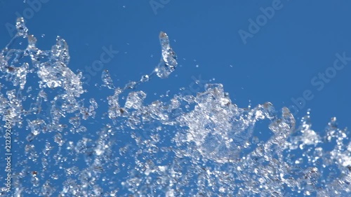 Close-up of sparkling fountain water splashes against clear blue sky. Refreshing droplets create dynamic abstract background representing freshness, summer, energy and motion
