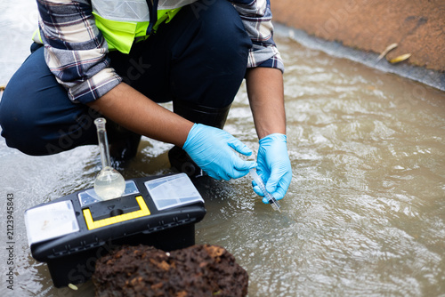 Environmental engineer collecting water sample from irrigation canal for agricultural water quality testing.