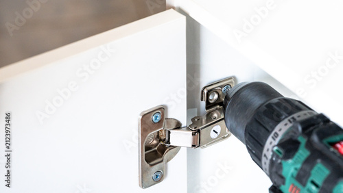 Bild auf Leinwand Close-up of a worker installing and adjusting cabinet door hinges using a power drill and screwdriver