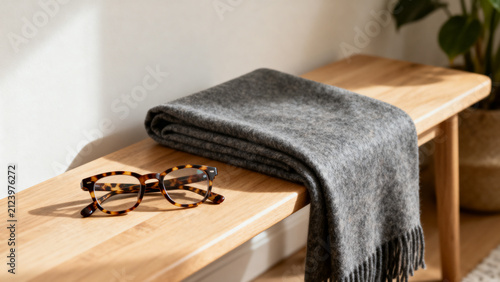 afterhours. Tortoiseshell eyeglasses and folded wool scarf on oak bench, cozy home lifestyle and fashion concept. lifestyle magazines.