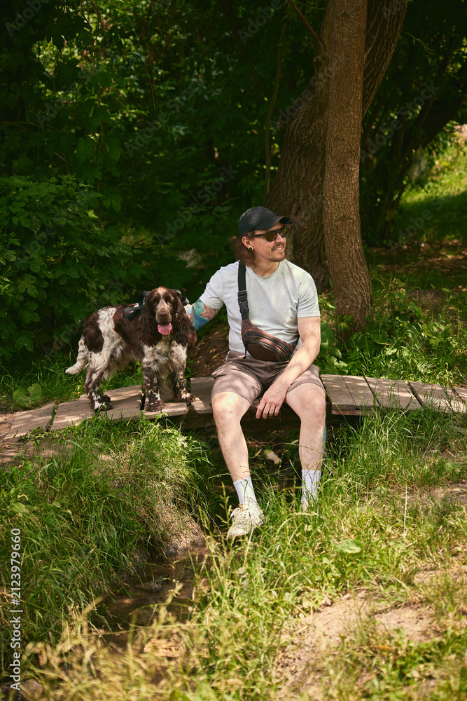 Obraz premium Man and dog resting together on log during peaceful forest hike. Concept of hiking rest break, outdoor pet friendship, slow nature lifestyle.