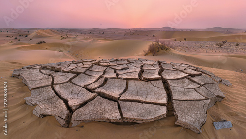 A vast desert landscape at dawn with cracked dry earth in the foreground representing drought.