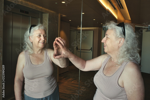 Quadro su tela Elderly woman touching mirror reflection as metaphor of self-awareness