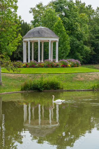 White pavilion in a blooming garden with a pond and a swan in the water. a round, shaded shelter in the Parc de l'Orangerie in Strasbourg.