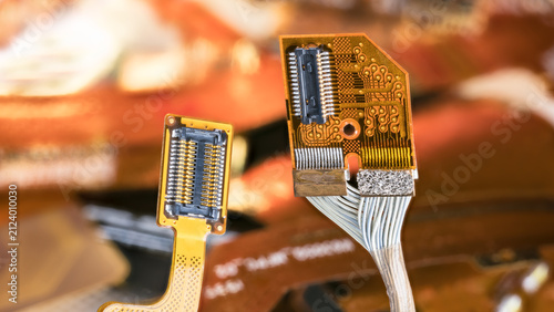 Closeup electronic flex connectors of cellphone, tablet or computer on blur background. Yellow flexible flat cable with contact pins and orange bendy printed circuit board with white electrical wires.