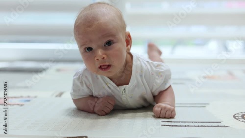 Adorable infant lying on tummy on a rug, looking curiously at the camera during tummy time at home. 4k footage.