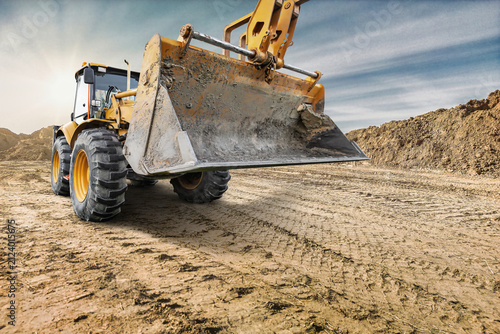 Heavy equipment is operating on a construction site to move dirt and materials during the day. The sun is shining on the work area