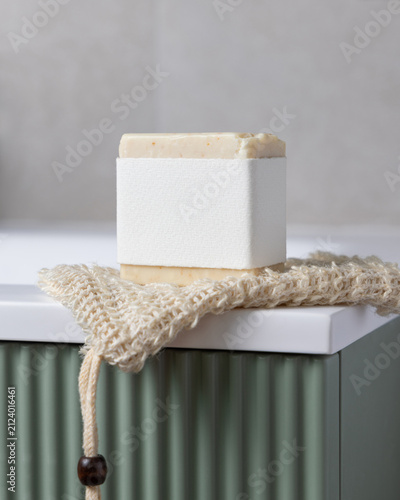 Solid soap bar with blank label mockup on soap saver bag on green bathroom vanity closeup