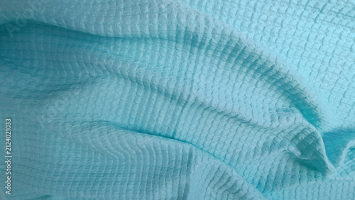Abstract close up of quilted light blue fabric with a stitched square grid creating a raised, tactile surface.