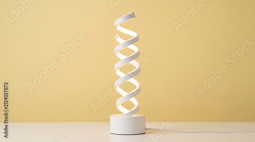 Modern white LED table lamp in a DNA-like helical spiral design, glowing on a minimalist desk against a solid pale yellow background. Minimalist home decor lighting fixture with a clean look.