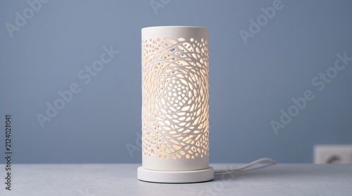 Modern white cylindrical table lamp with an intricate organic bird nest carved pattern, casting a warm glow against a muted blue background.