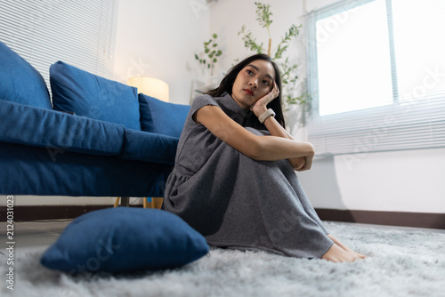 Young woman experiencing emotional sadness and depression, sitting alone on the living room floor, mental health struggle.