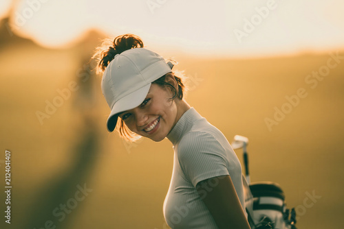 Smiling golfer walks on the course during golden hour with golf clubs in hand