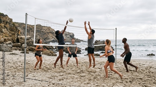 Diverse group of friends playing volleyball on a sandy beach near rocky cliffs