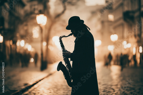 Musician plays saxophone on a quiet street while people walk by in the background