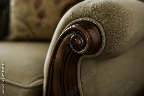 Upholstered sofa armrest featuring carved wooden scroll detail