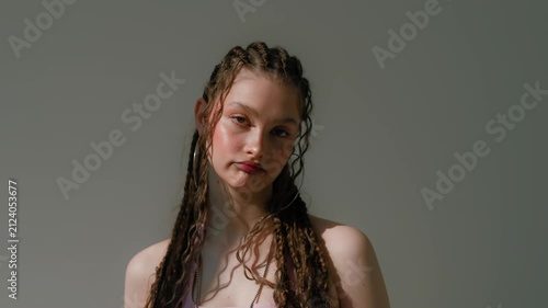 Calm young woman with braided hair, hoop earring, bare shoulders, and soft editorial studio lighting