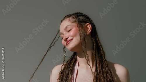 Young woman with braided hair and hoop earrings in pink top against sunlit gray background portrait