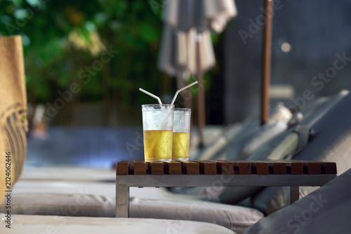 Close-up of two refreshing yellow cocktails or iced drinks with straws resting on a wooden table at a resort.
