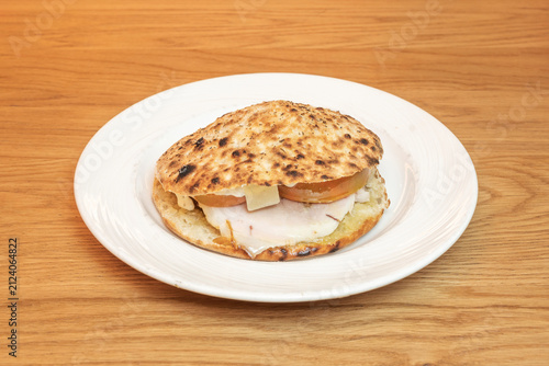 Bild auf Leinwand Toasted flatbread sandwich filled with sliced turkey, cheese, and tomato, served on a white plate over wood