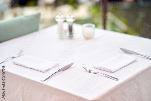 Close-up of an elegant restaurant table setting with a clean white tablecloth, neatly folded napkins, and shiny silverware cutlery.