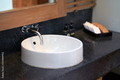 Modern bathroom interior featuring a round white ceramic washbasin sink on a sleek black countertop with a chrome faucet.
