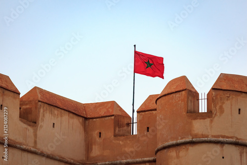 Foto Moroccan flag atop a fortress wall against a clear sky.