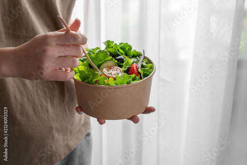 A woman holds a healthy vegetable salad in an eco-friendly takeaway bowl.