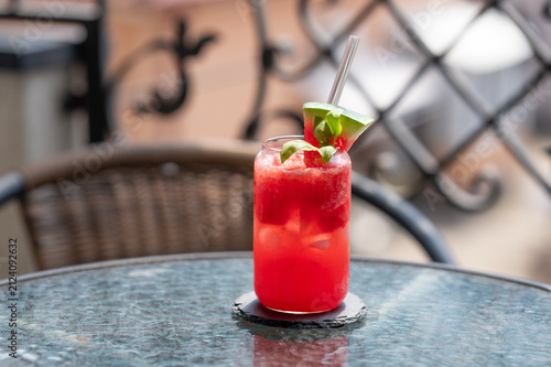 A watermelon mojito with ice and basil in a glass on a table in a sunny cafe.