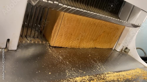 Closeup of artisan toast bread being sliced on a commercial bread slicing machine in a bakery. Fresh loaves move through professional equipment, precision cutting, and traditional bakery production.