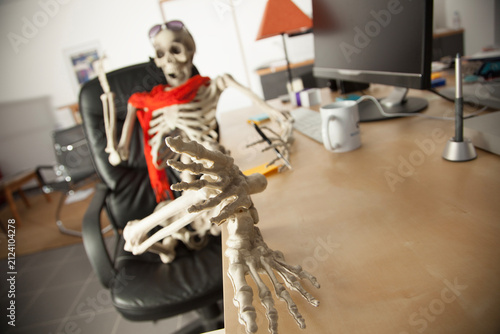 Obraz na płótnie Skeleton waiting at office desk reaching toward camera