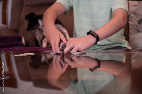 Teenage boy shuffling a deck of playing cards on a glass table at home while preparing for a card game with copy space