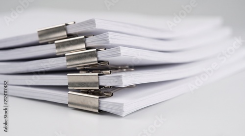 Stacked office paper sheets organized with metal binder clips on desk surface