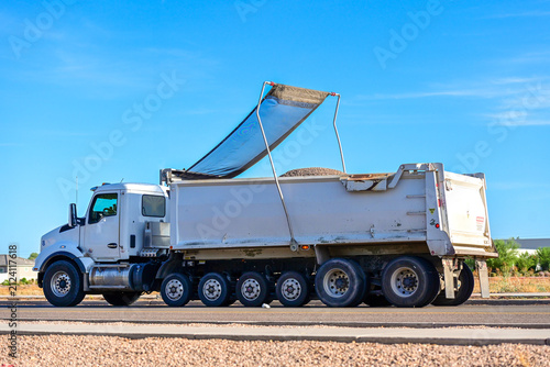 Foto Dump truck hauling aggregate with a retractable mesh tarp system on a roadway, i