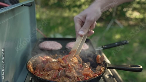 Person cooking vegetable and meat stew on a camping stove outdoors