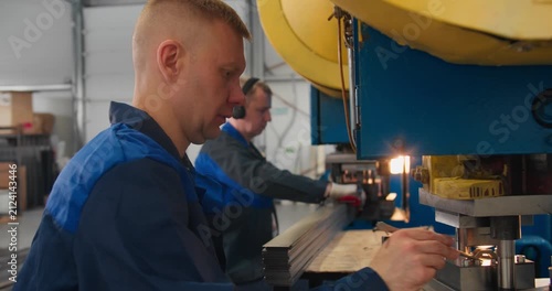 Production workers operating mechanical presses in a factory manufacturing metal parts from flat metal stock