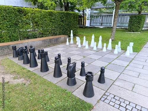Giant outdoor chess game with large black and white pieces on garden chessboard