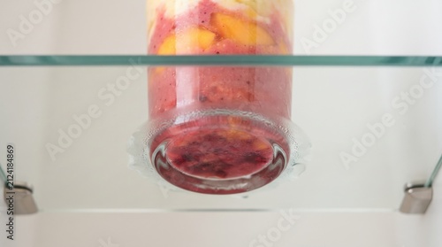A vibrant smoothie displays colorful layers of fresh fruits, with bright oranges and deep reds blending together. Perfectly chilled, it sits on a glass shelf, inviting anyone to enjoy the taste.