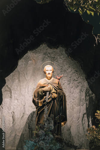 Obraz na plátne Statue of a saint in a cave-like setting with natural elements